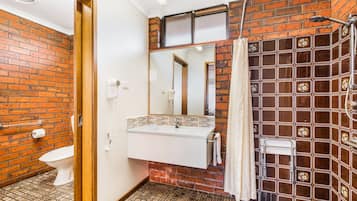Un baño con lavamanos blanco, un espejo, ducha y retrete.