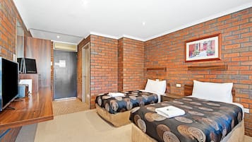 Una habitación de hotel con dos camas, un televisor y una pared de ladrillo.