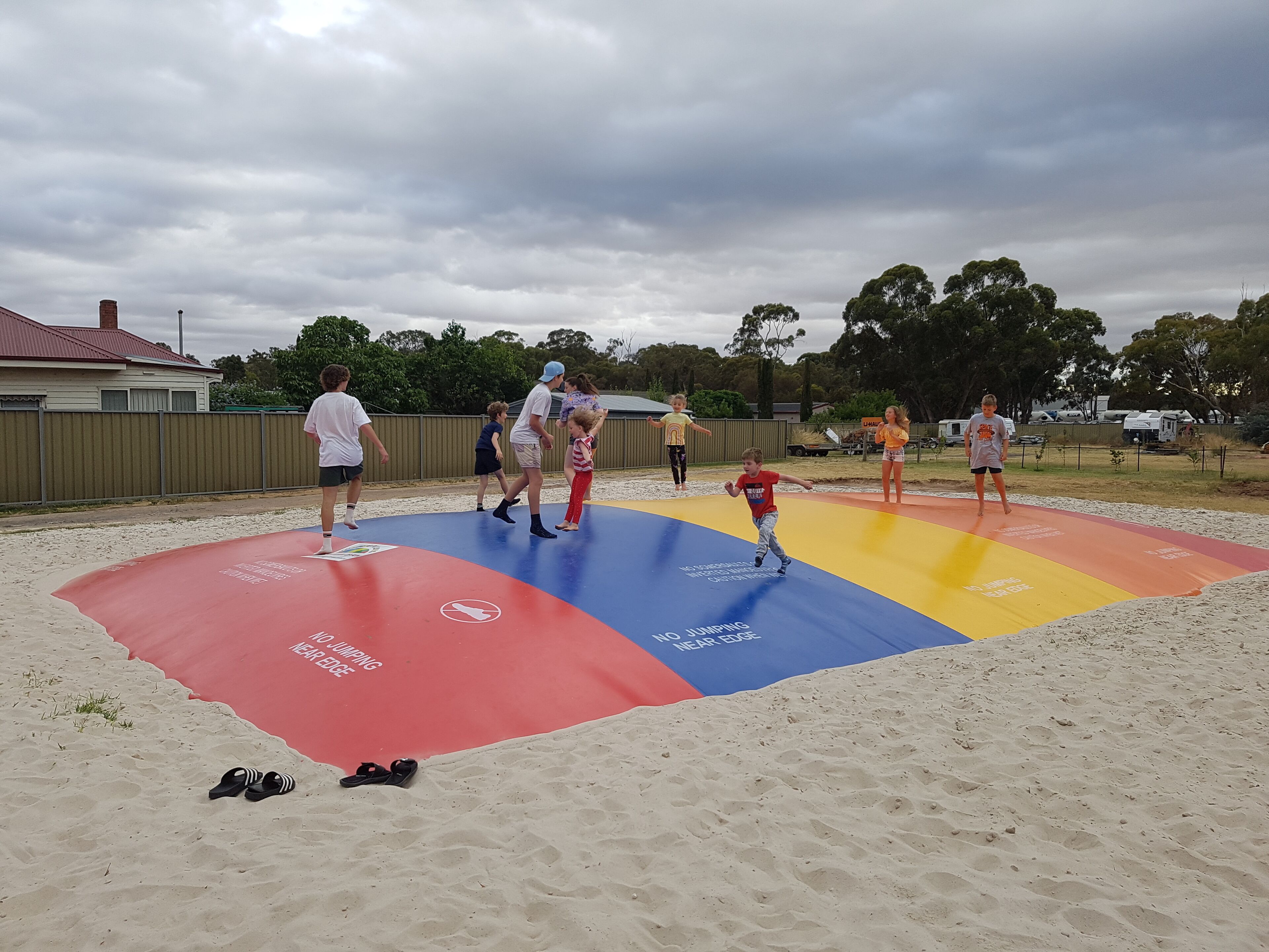 Un grupo de niños jugando en un arenero colorido con advertencias de seguridad.