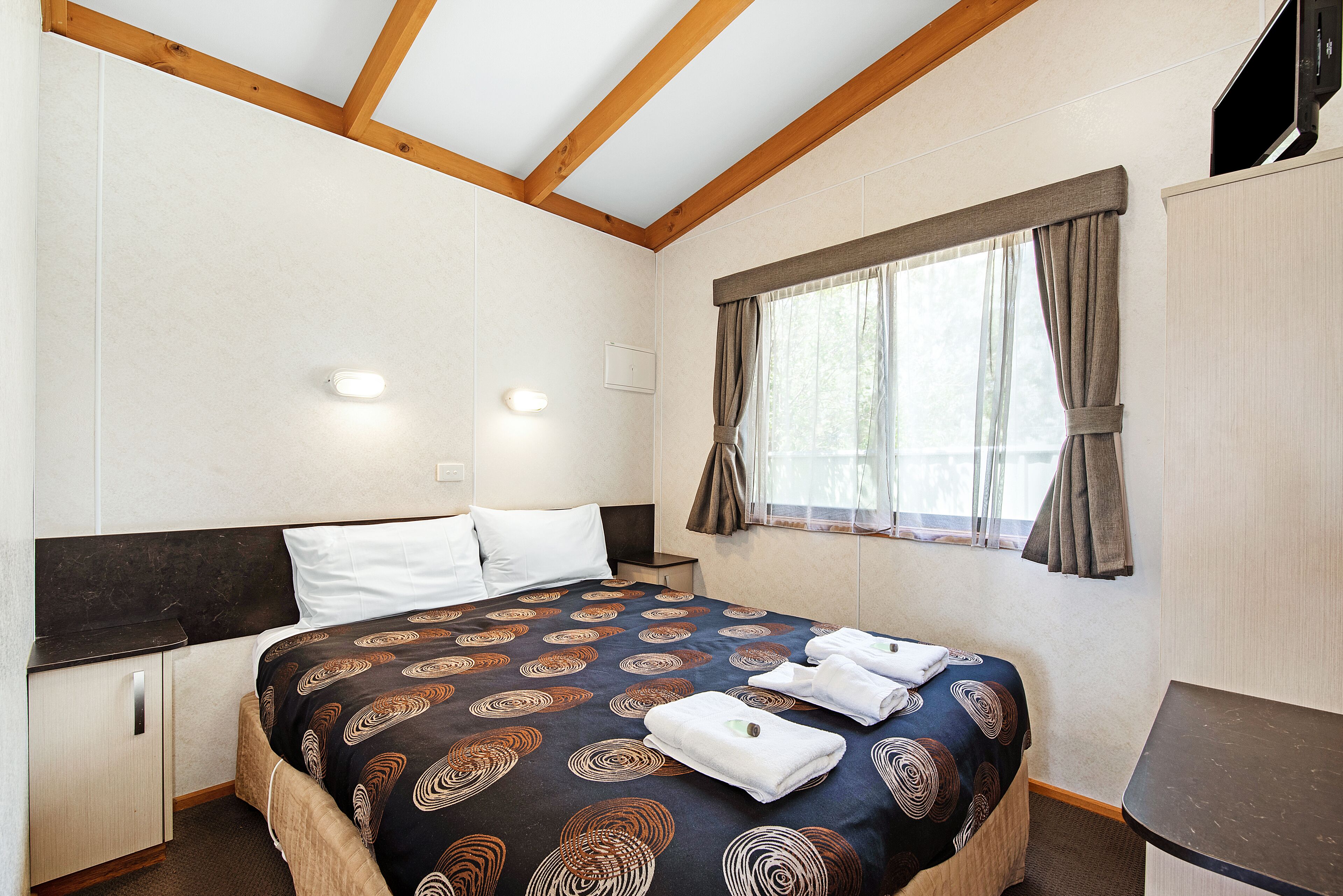 A bedroom with a bed, a nightstand, a wardrobe, and a window with curtains.