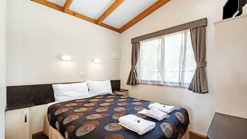 A bedroom with a bed, a nightstand, a wardrobe, and a window with curtains.