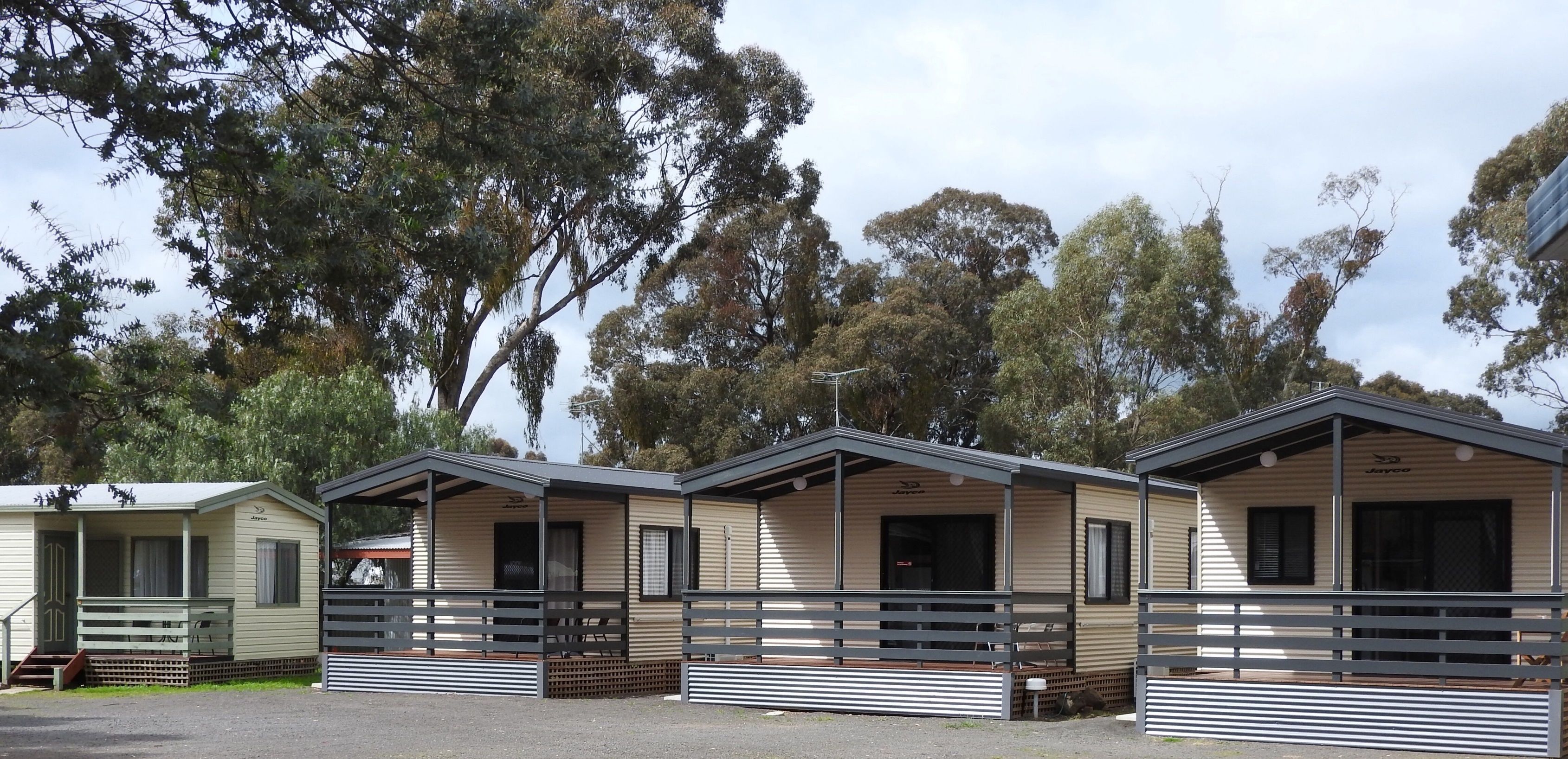 A row of mobile homes with a covered porch and a fenced area.