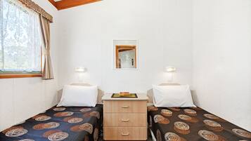 A small, clean room with two single beds, a wooden nightstand, a mirror, and two bedside lamps.