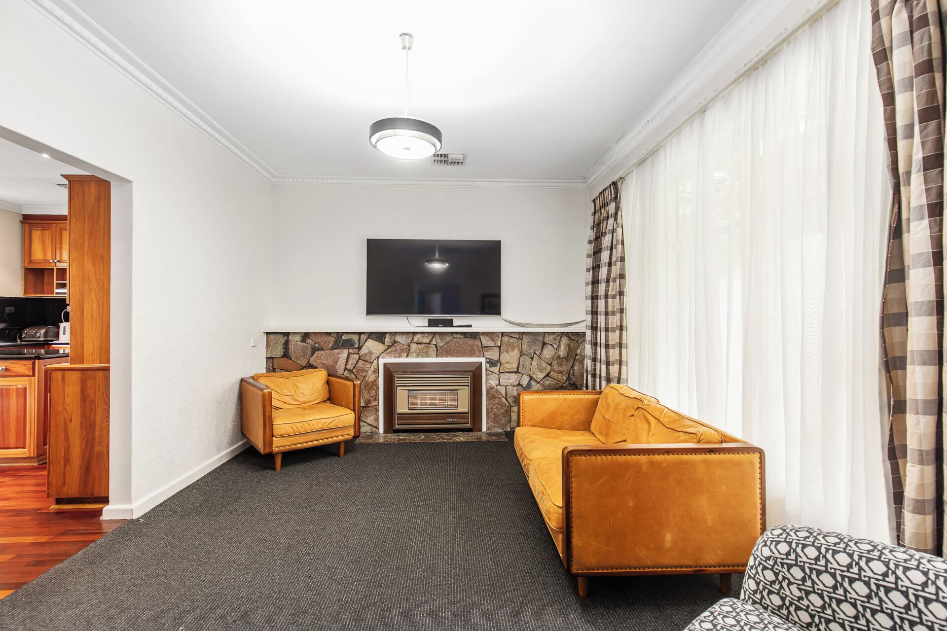 Een woonkamer met een stenen openhaard, een flatscreen televisie en twee gele banken.
