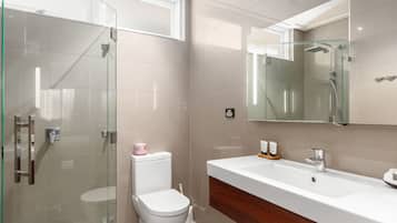 A modern bathroom with a glass-enclosed shower, a white toilet, and a large white sink with a wooden cabinet below.