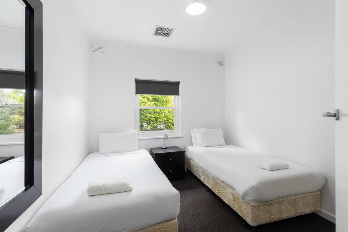 Une petite chambre propre, avec deux lits simples, une petite table et une fenêtre donnant sur un paysage verdoyant.