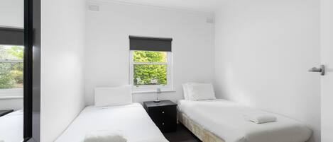 Une petite chambre propre, avec deux lits simples, une petite table et une fenêtre donnant sur un paysage verdoyant.