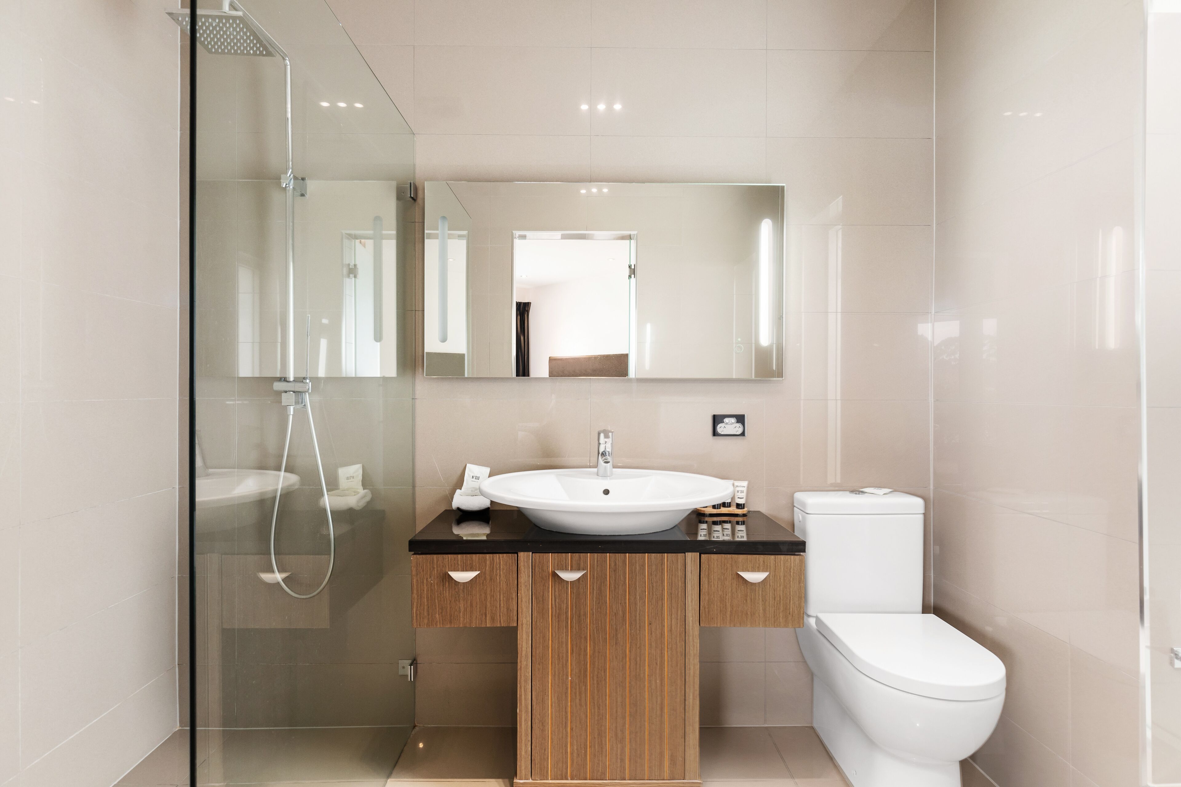 Ein modernes Badezimmer mit einer gläsernen Dusche, einem Holzwaschtisch mit weißem Waschbecken und einer weißen Toilette.