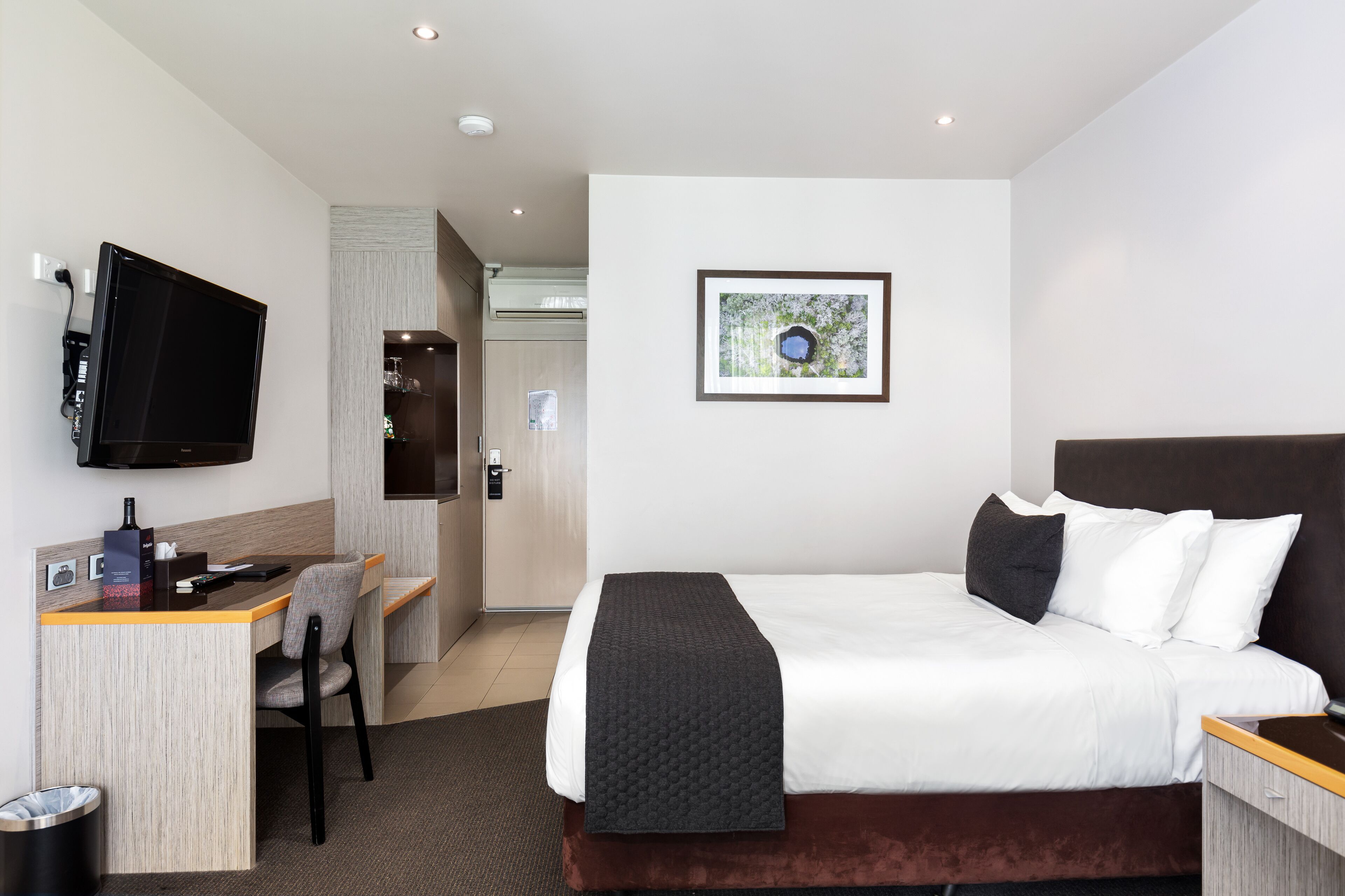A hotel room with a bed, a desk, a chair, a television, and a framed picture on the wall.