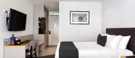 A hotel room with a bed, a desk, a chair, a television, and a framed picture on the wall.