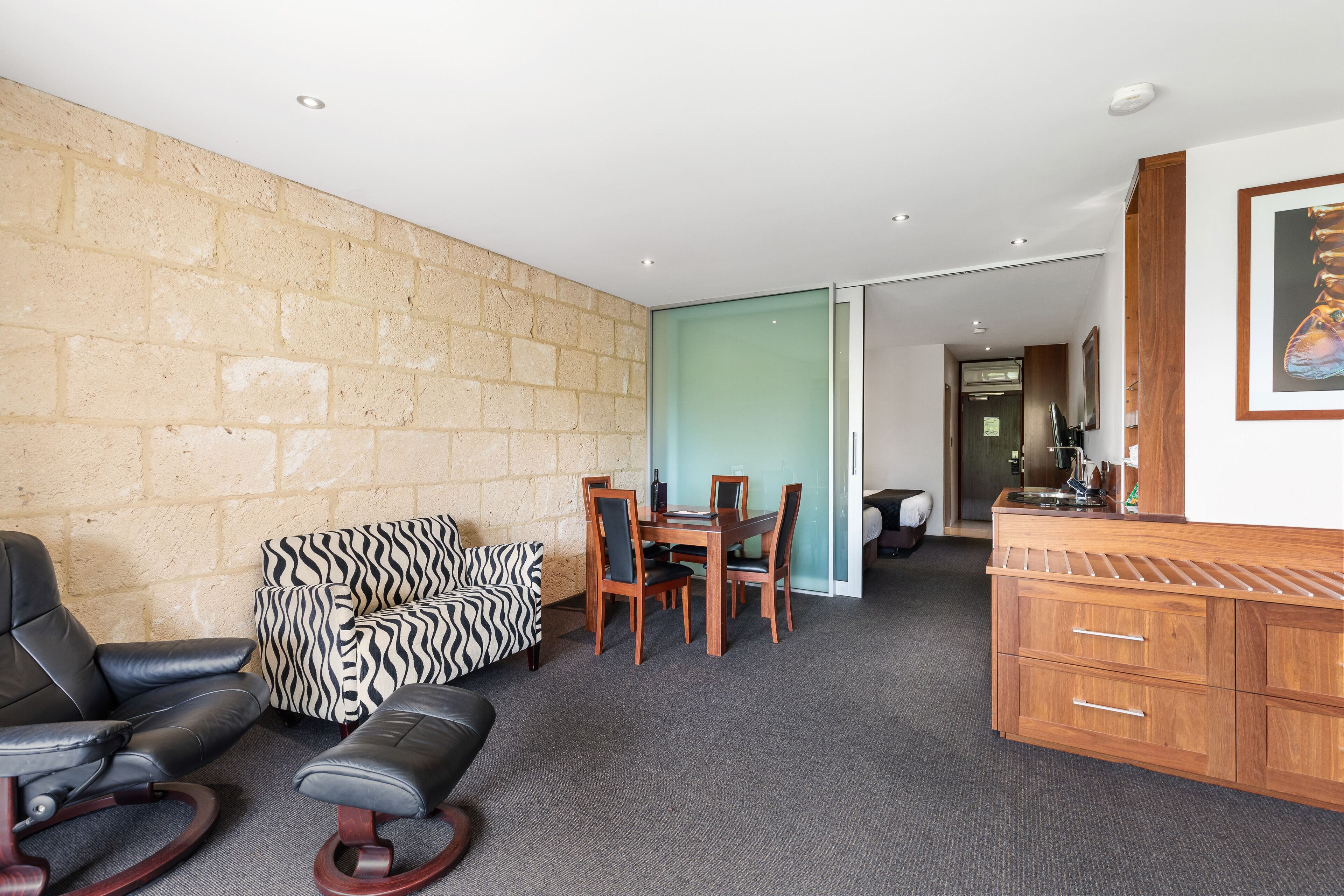 Ein Zimmer mit Backsteinwand, einem zebra-gemusterten Sofa, einem Esstisch mit Stühlen, einem Holzschrank und einem gerahmten Bild an der Wand.