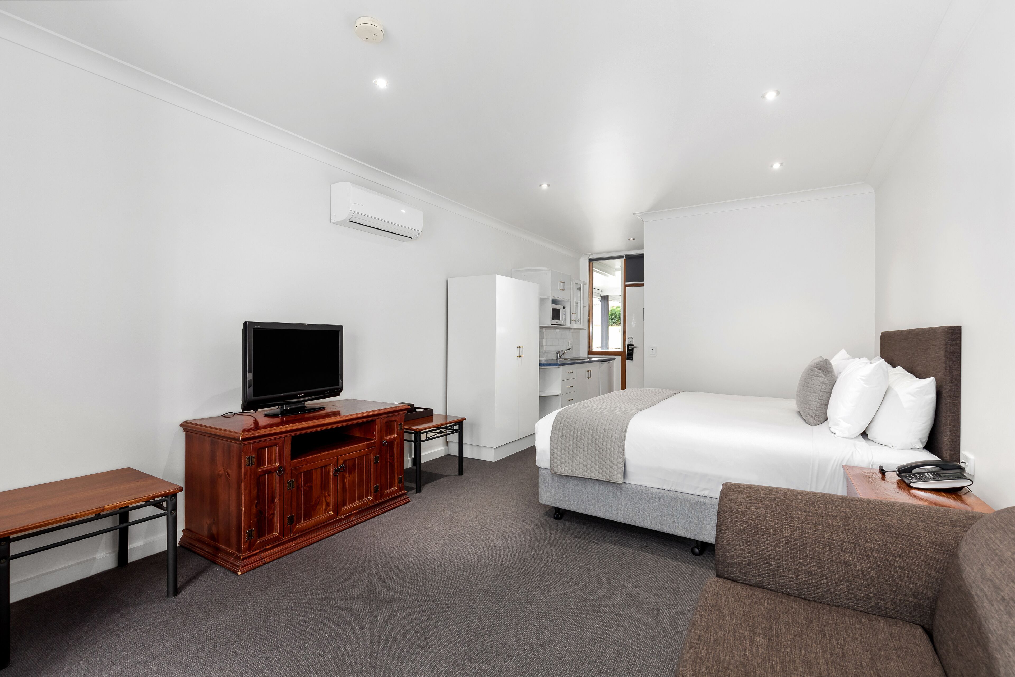 A hotel room with a bed, a TV, a wooden cabinet, a desk, and a small kitchenette.
