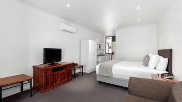 A hotel room with a bed, a TV, a wooden cabinet, a desk, and a small kitchenette.
