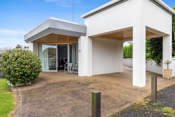 Una casa moderna con un porche cubierto, un arbusto grande y un letrero con el número 27.