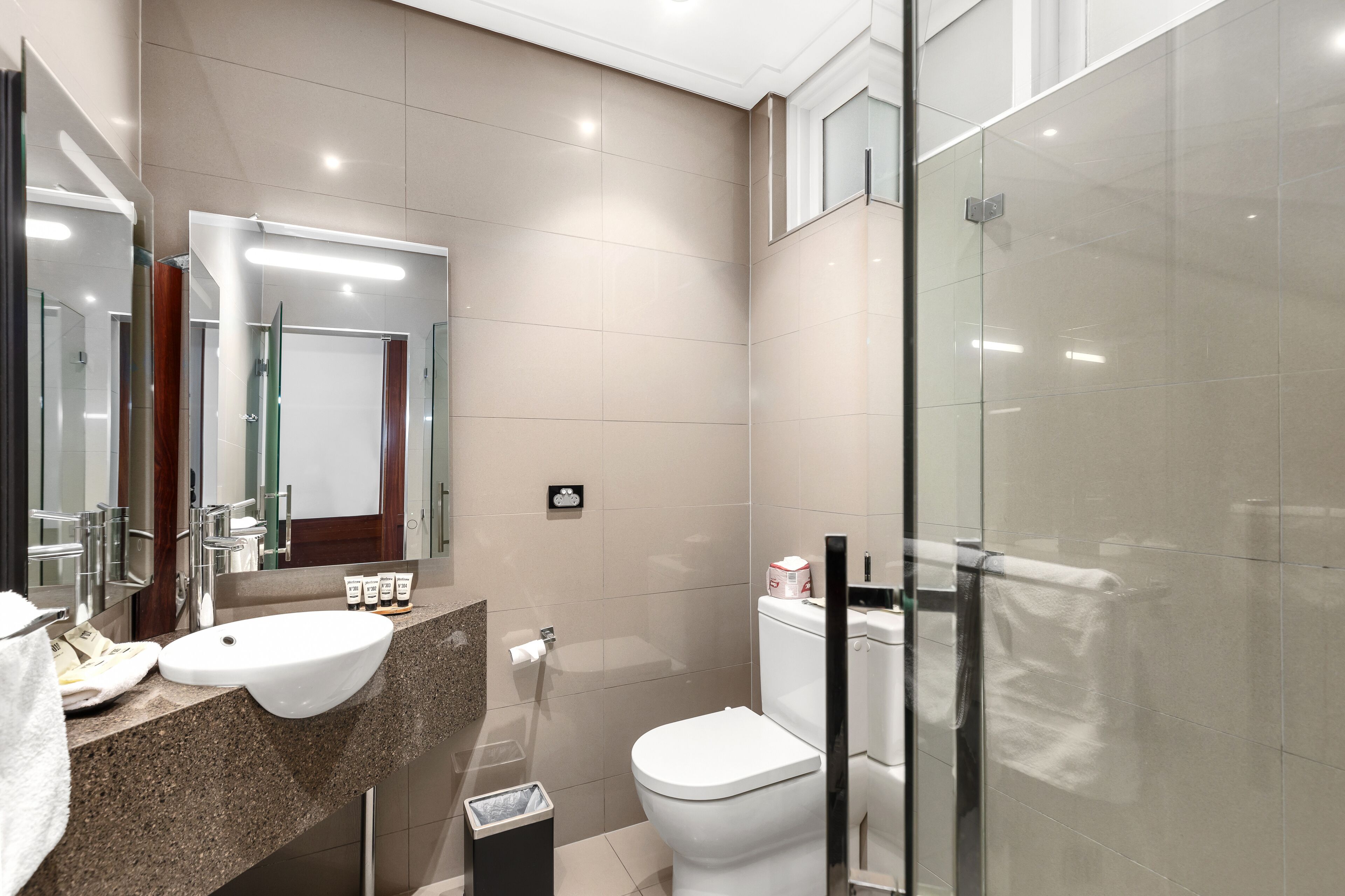 A modern bathroom with a sink, mirror, toilet, and glass shower enclosure.