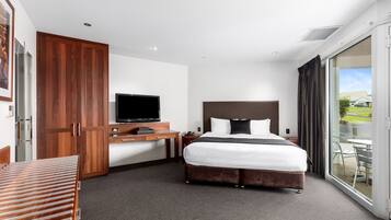 Una habitación de hotel con cama, escritorio, televisor y puerta corrediza de vidrio a un espacio exterior.
