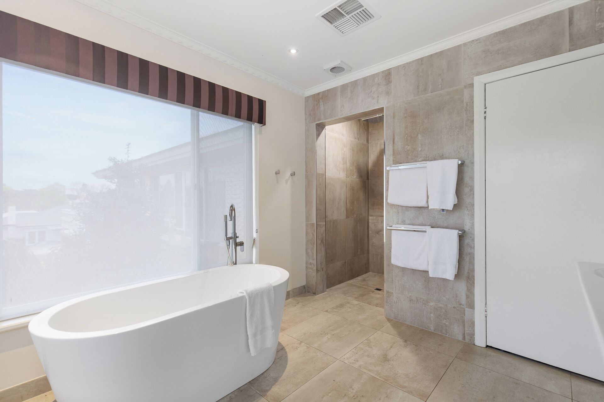 A modern bathroom with a freestanding bathtub, a shower enclosure, and a large window providing a view of the outside.
