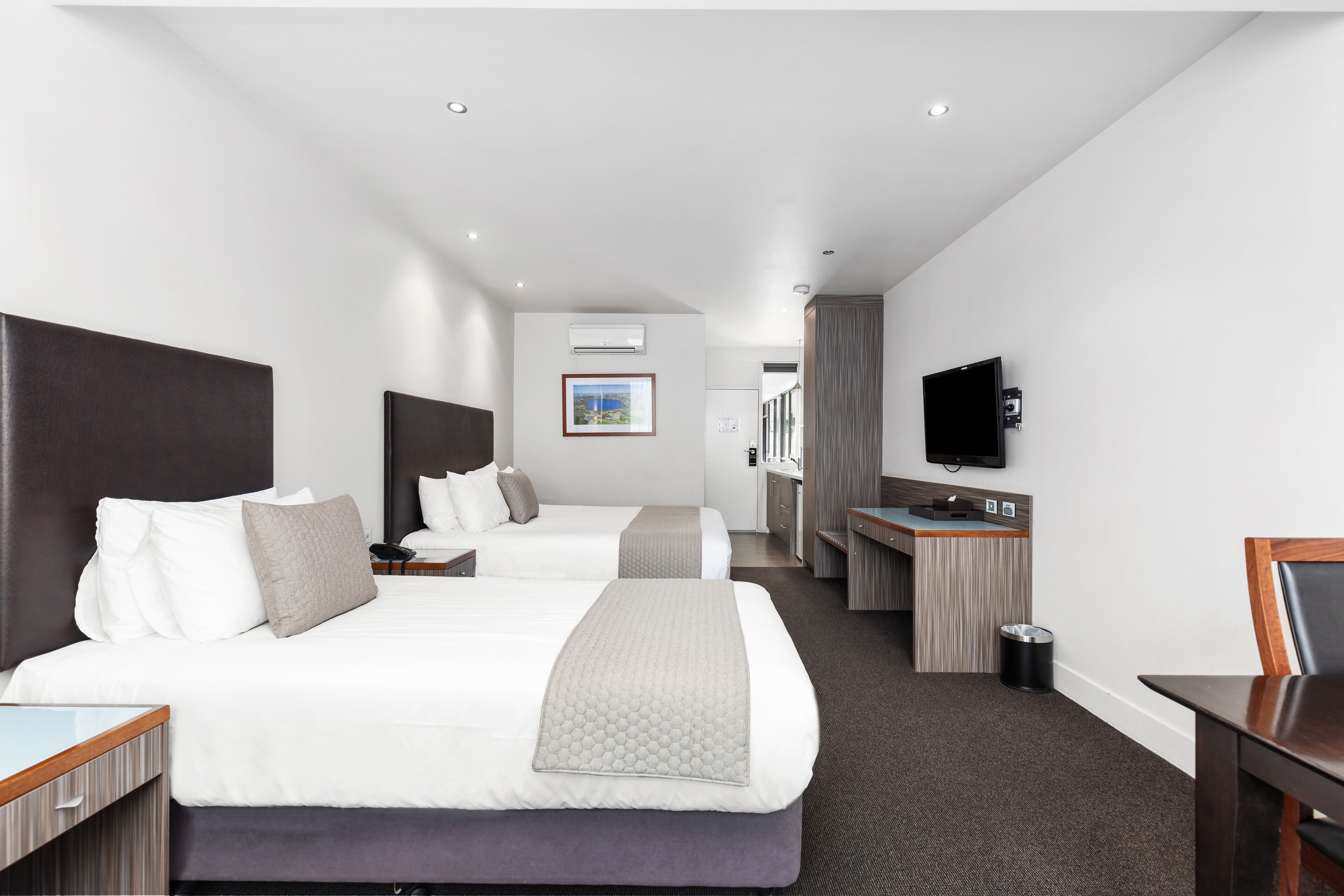 Een hotelkamer met twee bedden, een bureau, een televisie en een prullenbak.