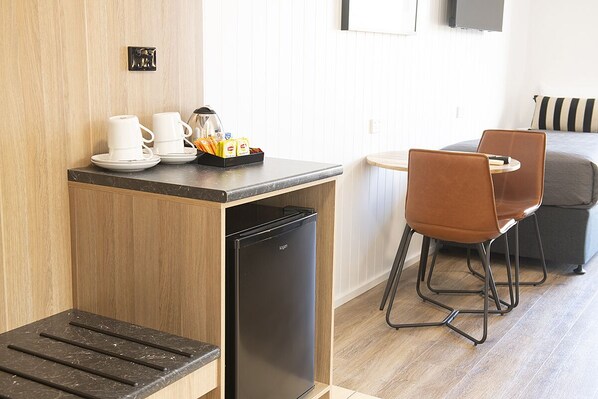 Cocina compacta equipada con refrigerador, cafetera y juego de té. Hay un comedor con mesa y sillas.