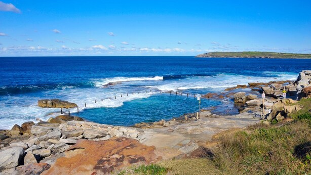 A rocky coastal landscape with a clear view of the ocean and a distant shoreline. - Southend Hotel (Maroubra)