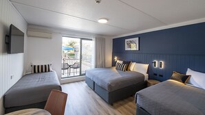 A hotel room with two single beds, a sofa bed, a dining table, and a balcony with a view. - Southend Hotel (Maroubra)