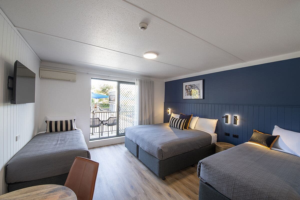 A hotel room with two single beds, a sofa bed, a dining table, and a balcony with a view.