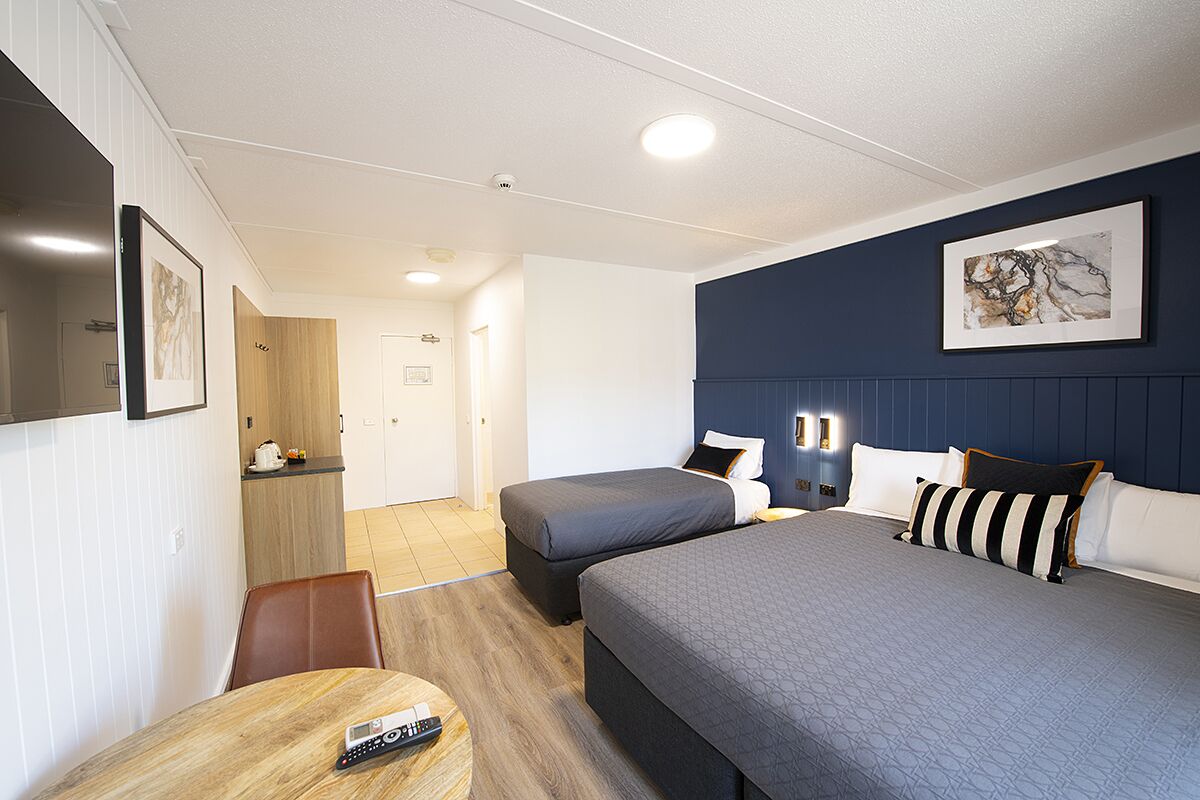 A hotel room with two beds, a dining table, a TV, and a painting on the wall.