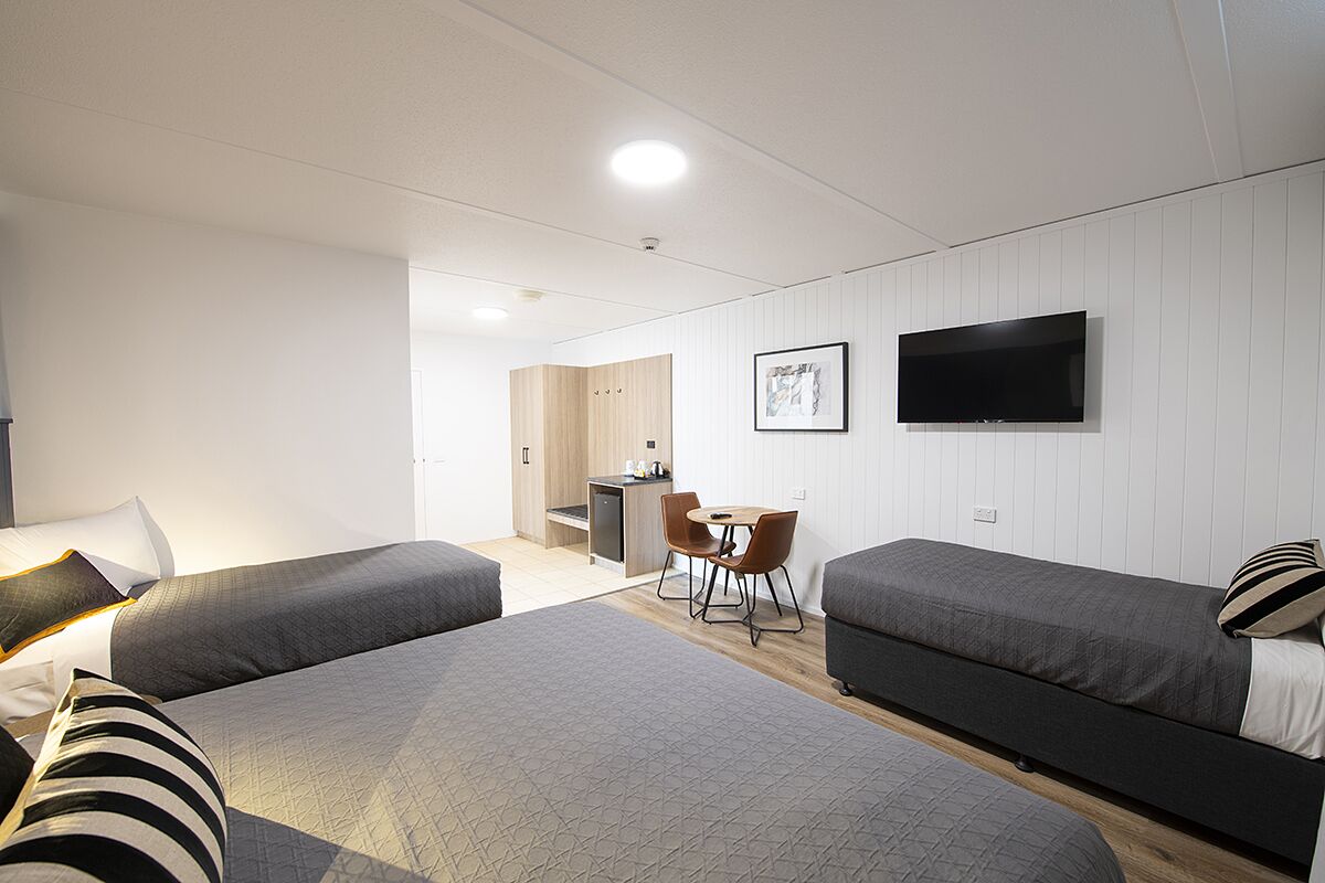 Una habitación de hotel con dos camas, un escritorio, una silla, un televisor y un kitchenette.