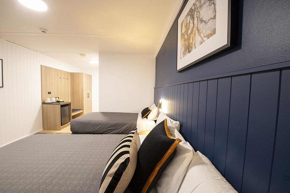 A hotel room with two beds, a small kitchenette, and a framed artwork on the wall.