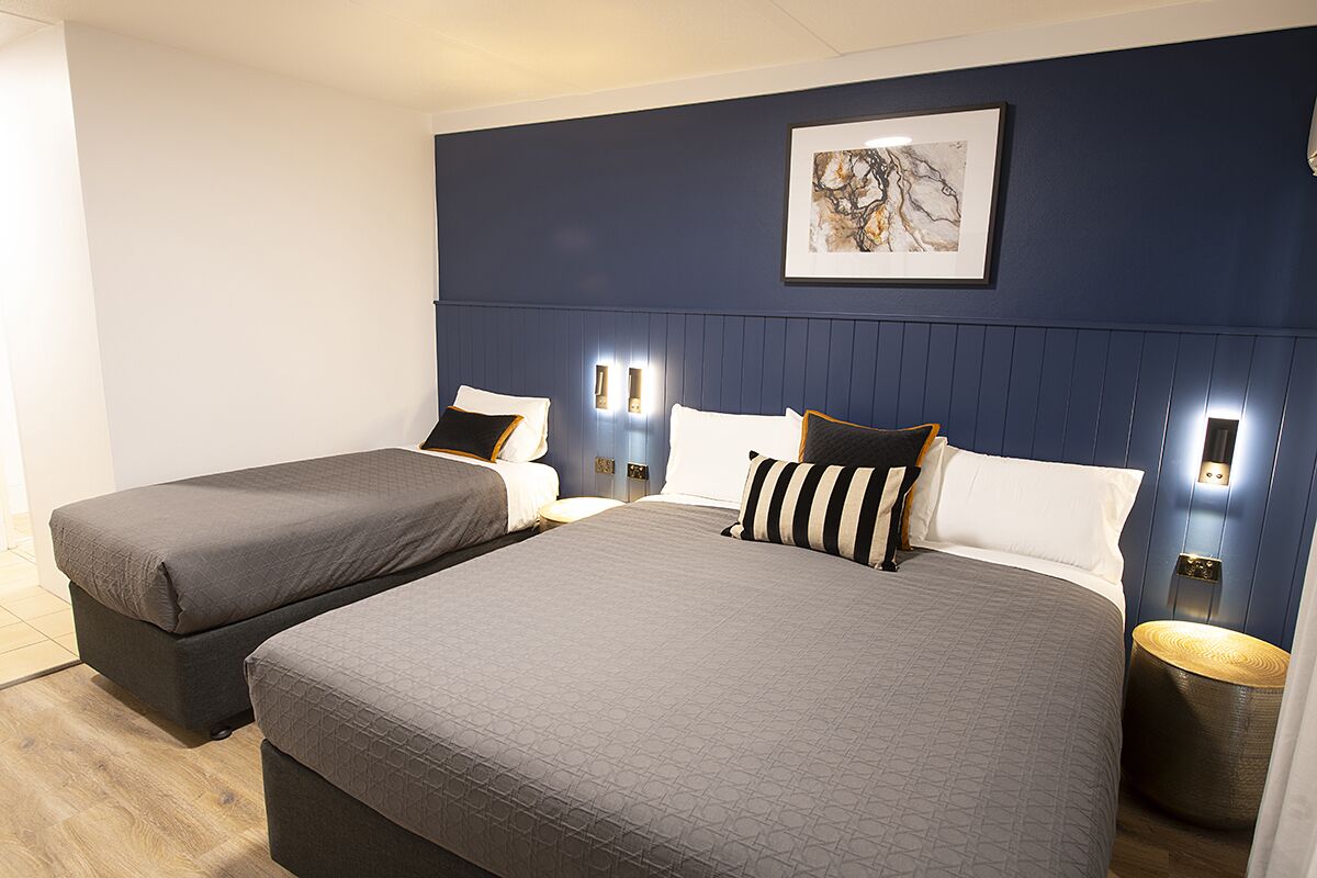 Une chambre d’hôtel avec deux lits, un mur d’accent bleu foncé, une œuvre d’art encadrée et des lampes de chevet.
