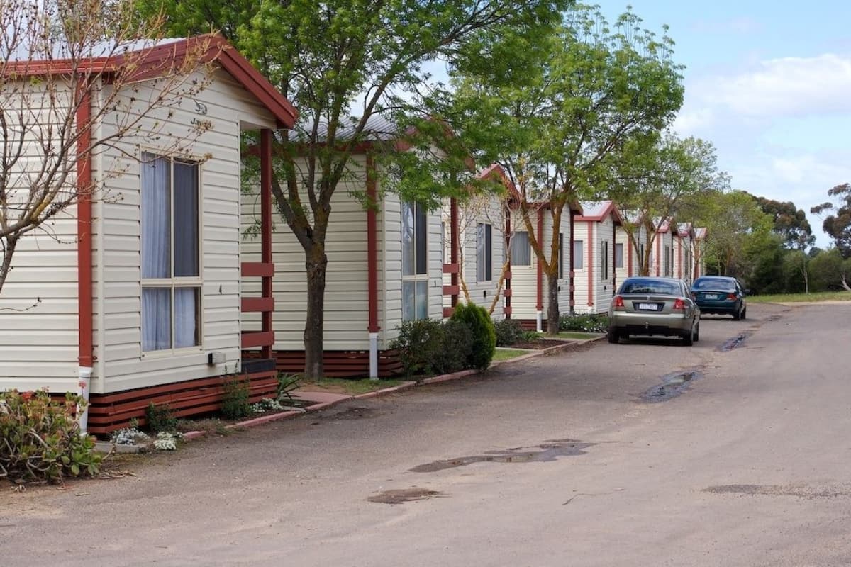 A row of mobile homes with a paved driveway and parked cars.