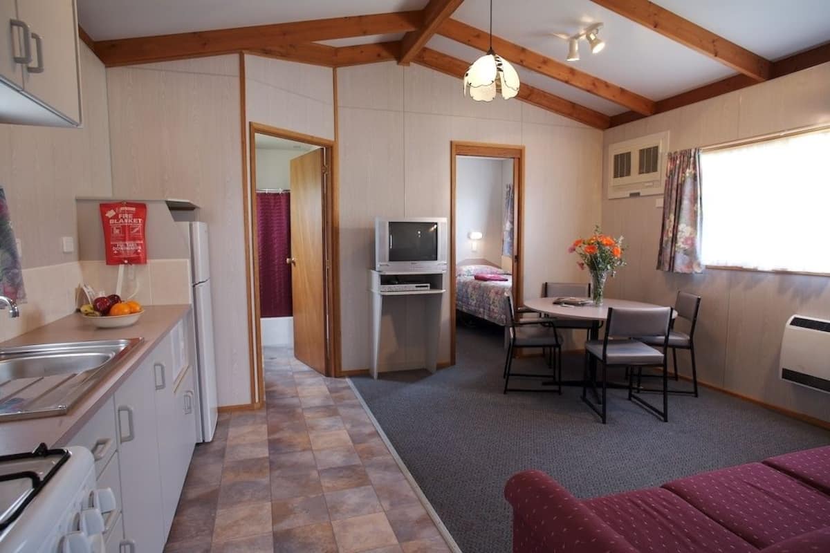 A compact kitchen with a sink, stove, and a small refrigerator. There is a dining area with a table and chairs, and a television in the corner.