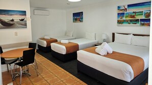 Quarto de hotel com duas camas de solteiro, uma cama de casal, área de refeições com mesa e cadeiras, e obras de arte nas paredes.