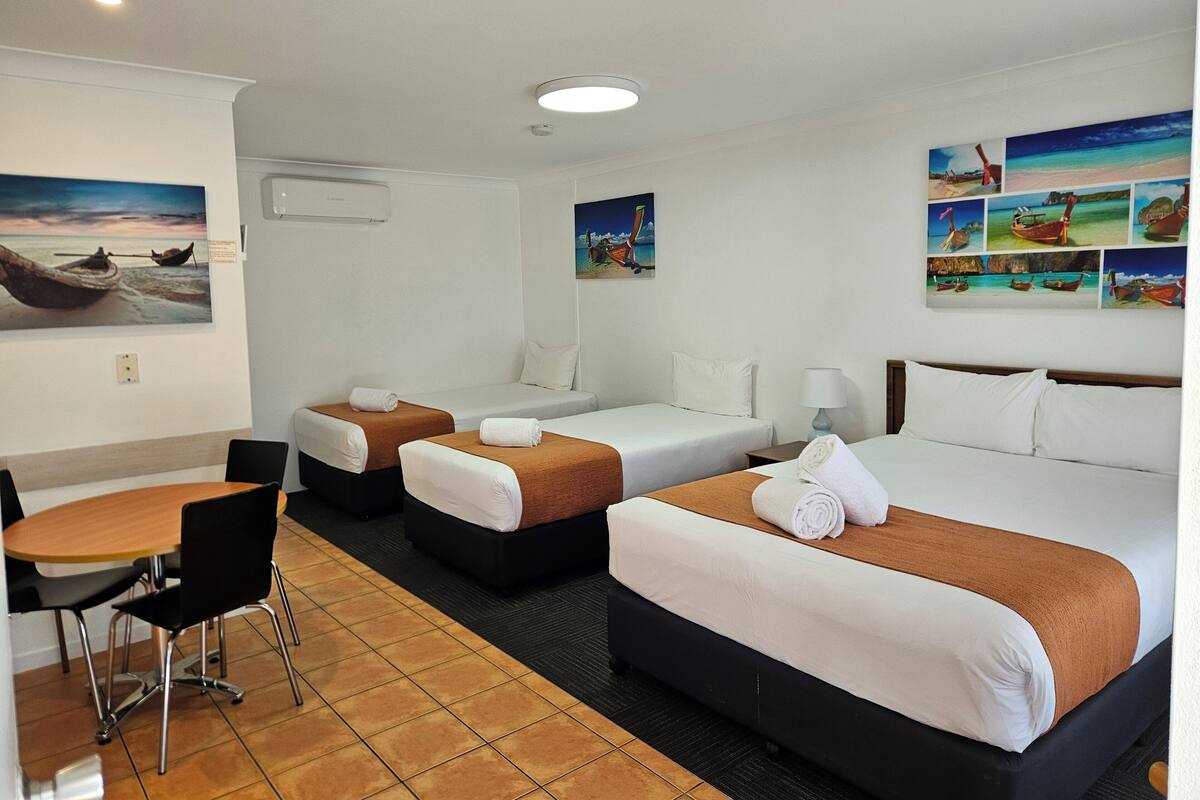 A hotel room with two single beds, a double bed, a dining area with a table and chairs, and artwork on the walls.