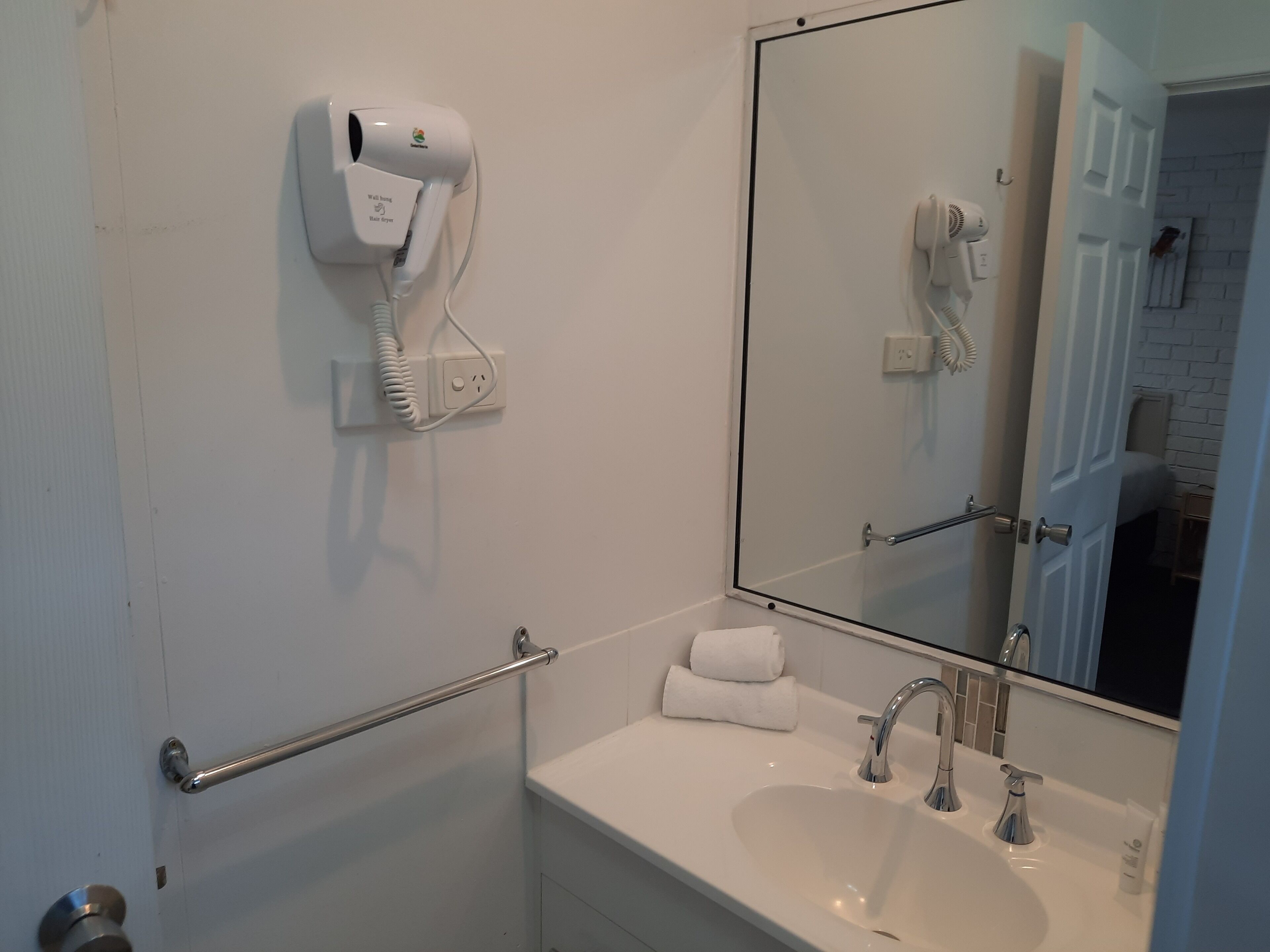 A bathroom with a white sink, a mirror, a hairdryer, and a towel rack.