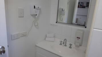 Un baño con lavamanos blanco, dos grifos, un espejo, un secador de pelo y una toalla.