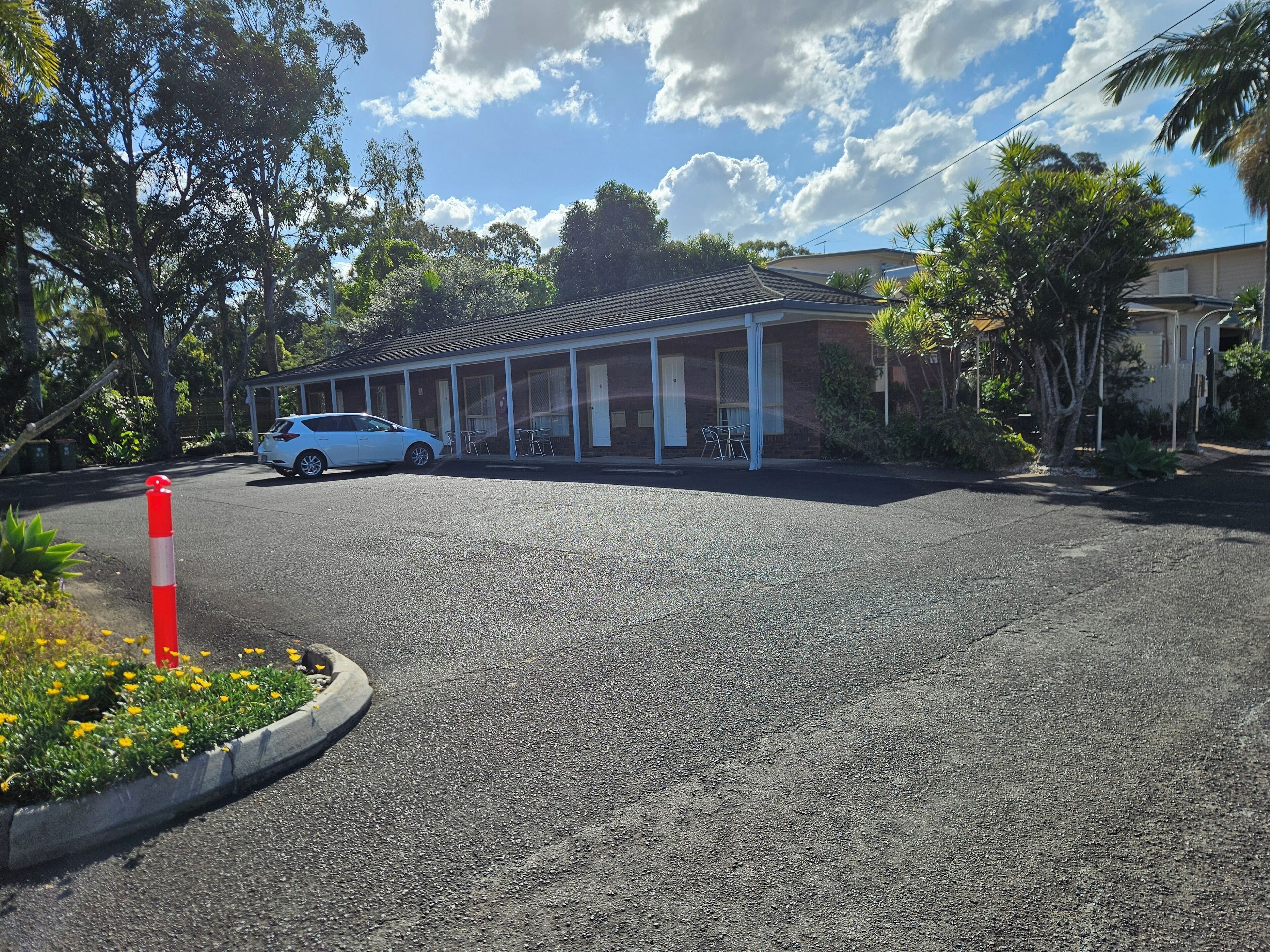 Un motel con zona de estacionamiento techada, un coche blanco estacionado en el interior y un cono de tráfico rojo y blanco en primer plano.