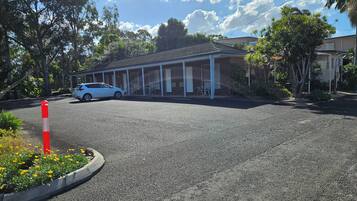 Un motel con zona de estacionamiento techada, un coche blanco estacionado en el interior y un cono de tráfico rojo y blanco en primer plano.
