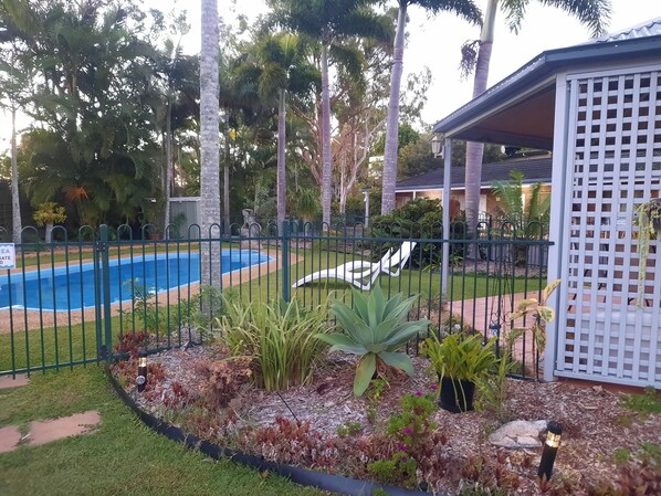 Un jardin à l’arrière de la maison, avec une piscine, entouré d’une clôture et agrémenté de différentes plantes.