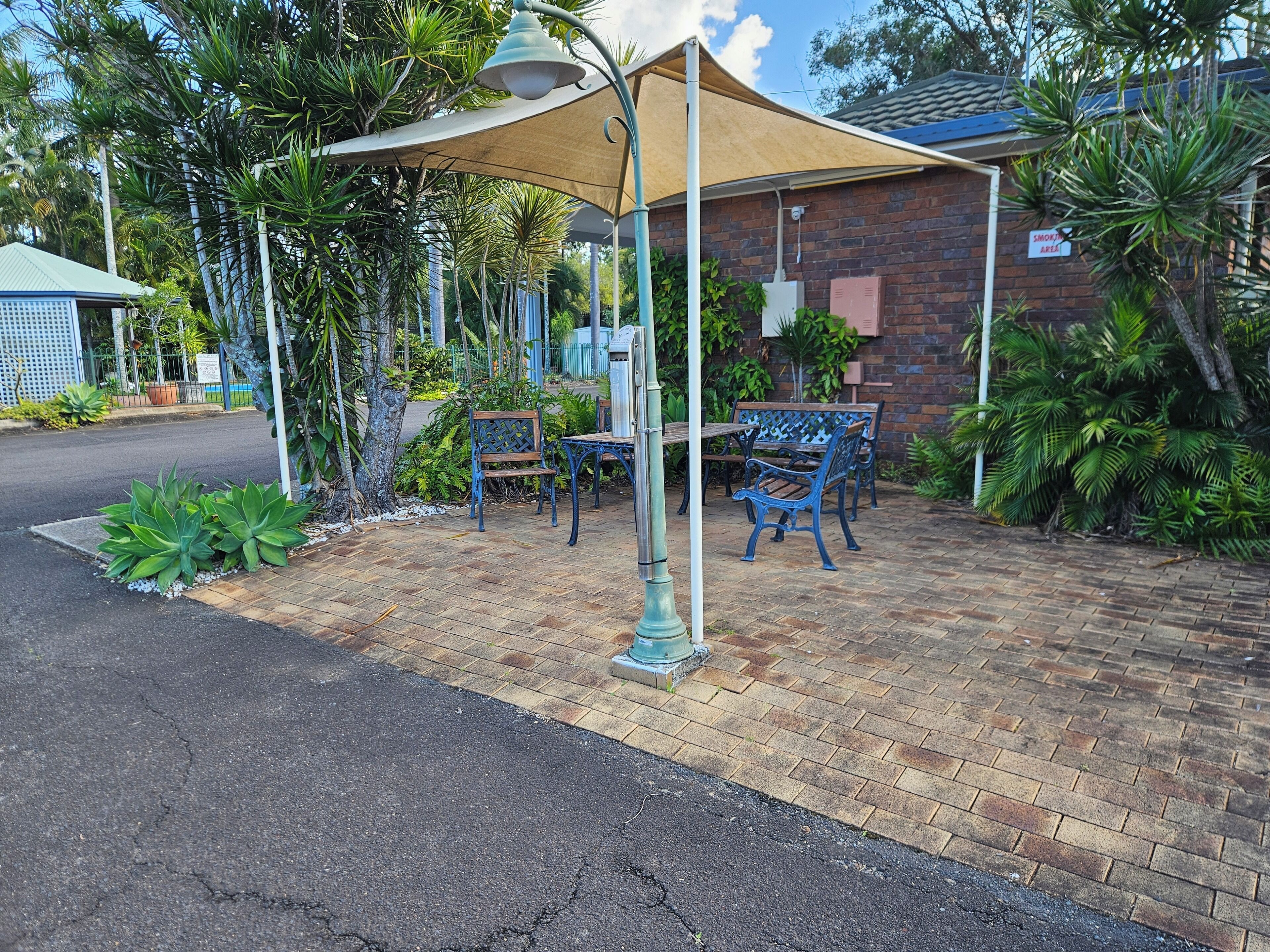 A patio area with a brick floor, outdoor seating, and a shaded area with a lamp post.