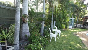 Um jardim com cerca de madeira, palmeiras e uma mesa e cadeiras brancas ao ar livre.