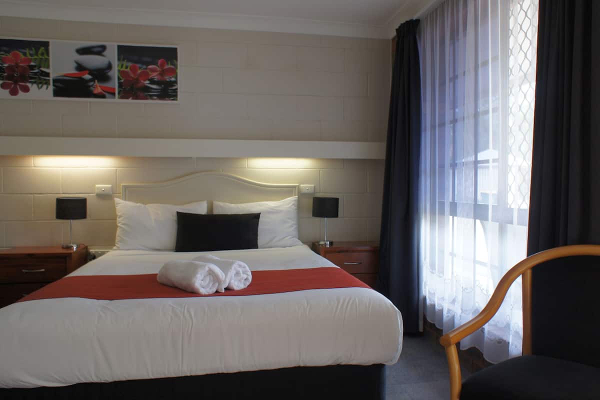 A hotel room with a neatly made bed, two bedside tables with lamps, a chair, and a window with curtains.