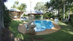 A swimming pool with a stone sculpture in the center, surrounded by a well-maintained lawn and palm trees.