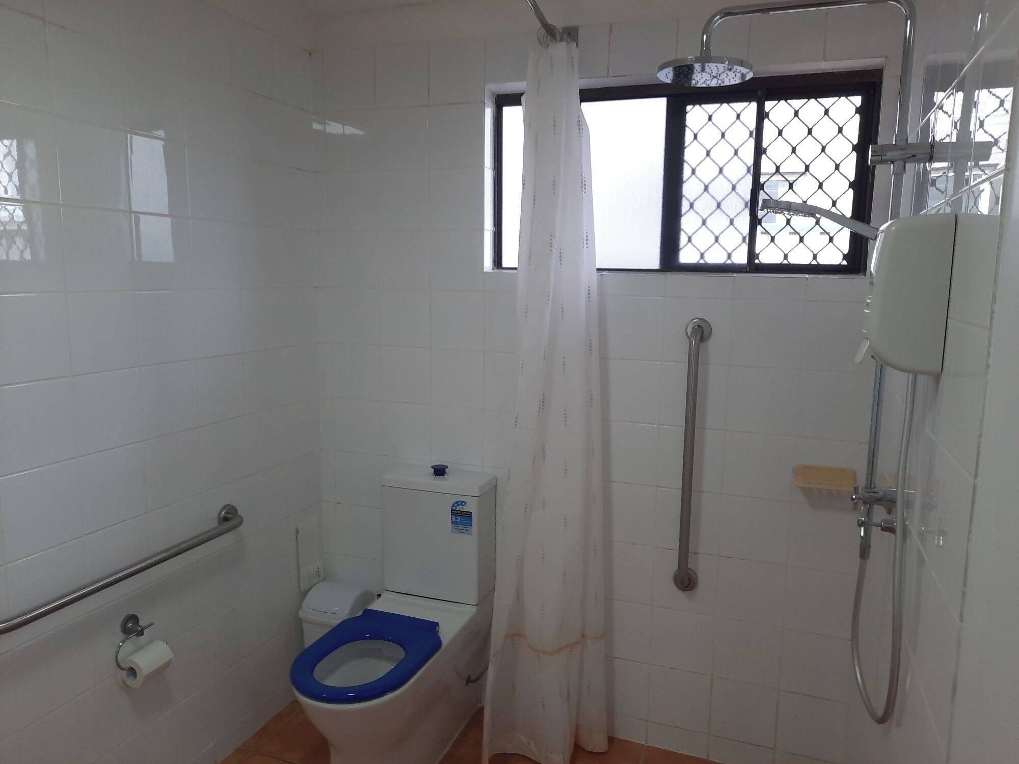 Casa de banho com sanita, chuveiro e janela com grade de metal.