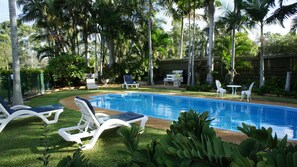 Une piscine entourée de chaises longues blanches, un espace barbecue et une végétation luxuriante.