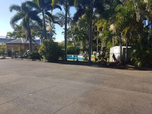 Un parking avec un espace piscine, entouré de palmiers et d’une clôture.
