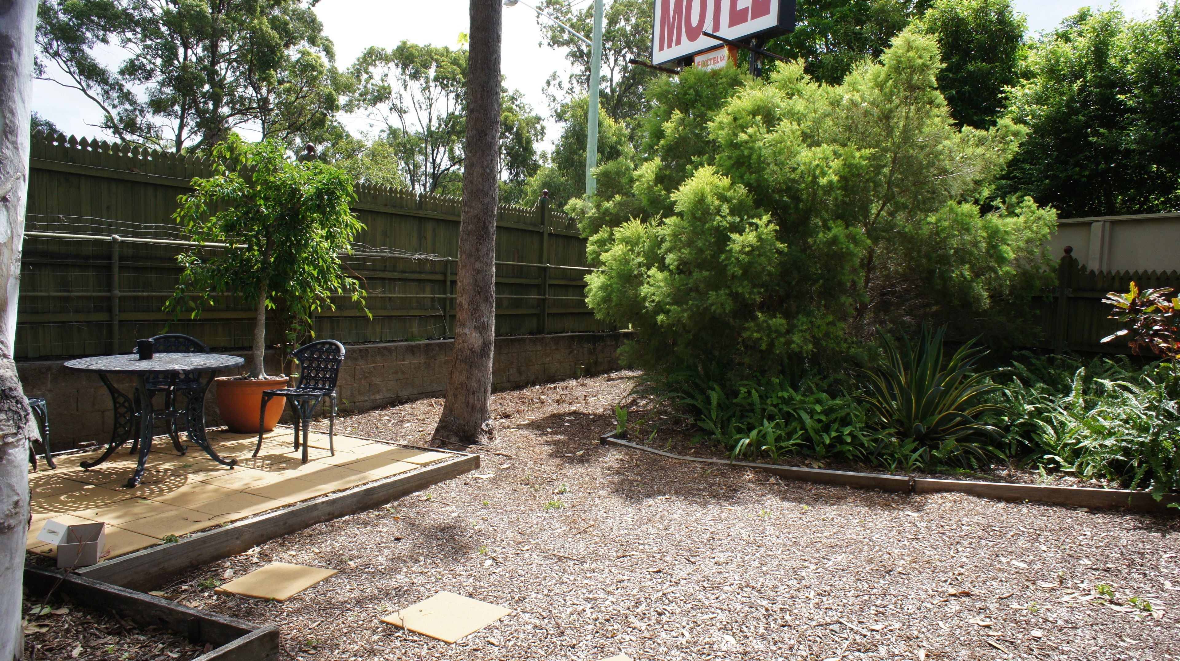 Un patio con mesa y sillas, rodeado por una valla de madera y varias plantas.