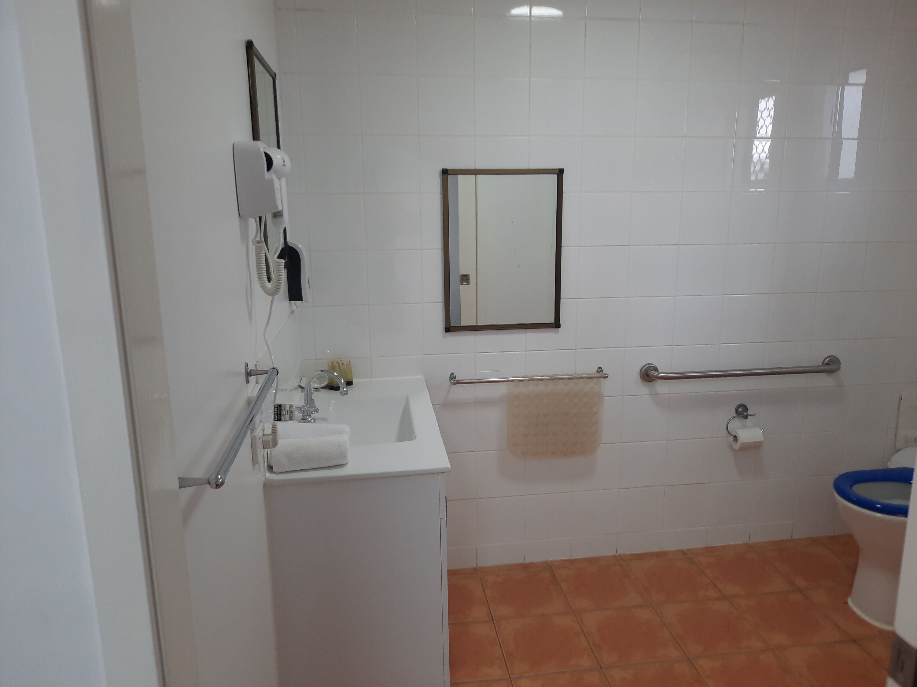 A bathroom with a white sink, a mirror, a towel rack, a toilet, and a hand dryer.