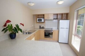 A compact kitchen with a microwave, oven, and refrigerator, a sink, and a potted plant. - Alhambra Oaks Motor Lodge (Dunedin)