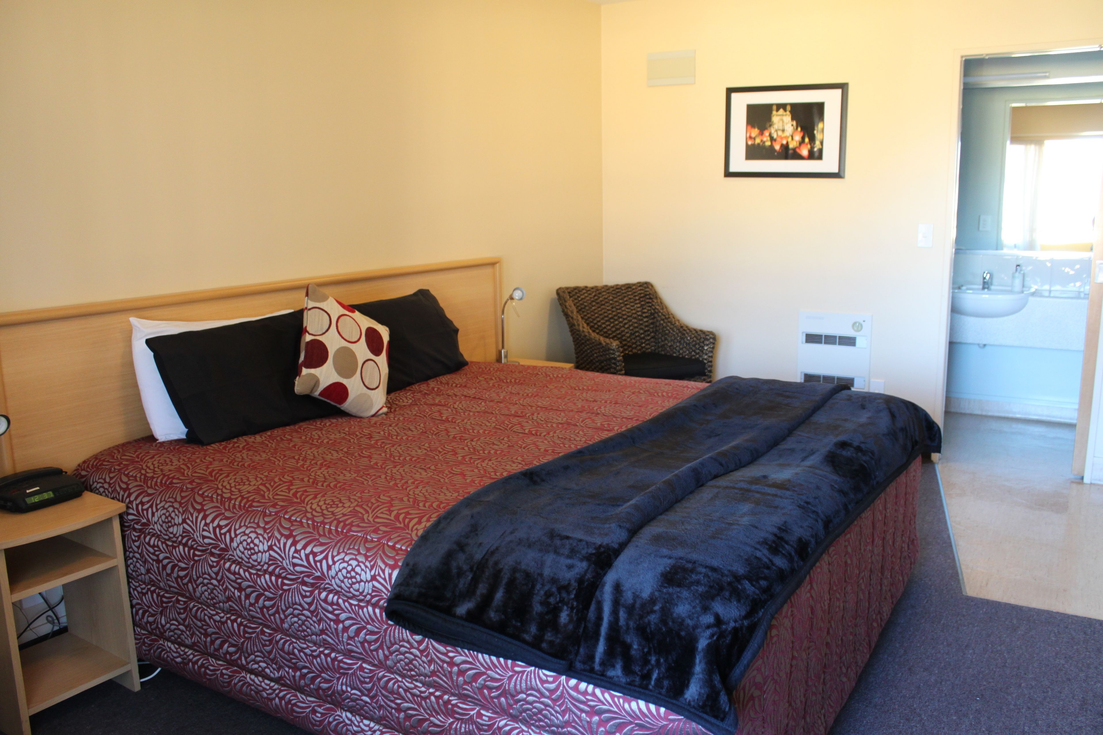 A hotel room with a large bed, a chair, a bedside table, and a wall-mounted picture.